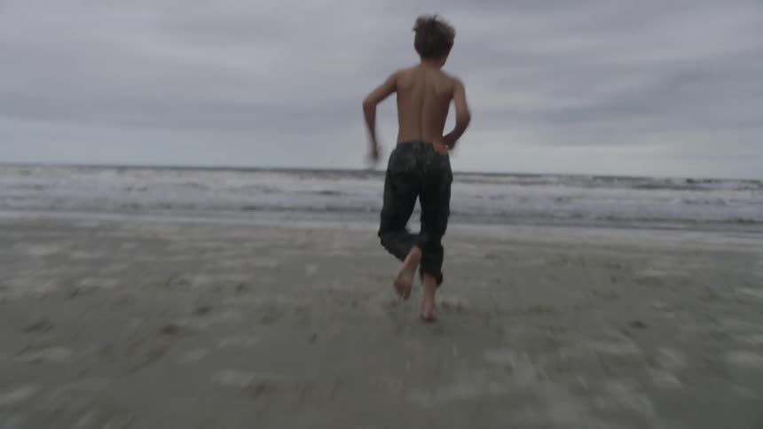 Boy runs toplessinto ocean past man