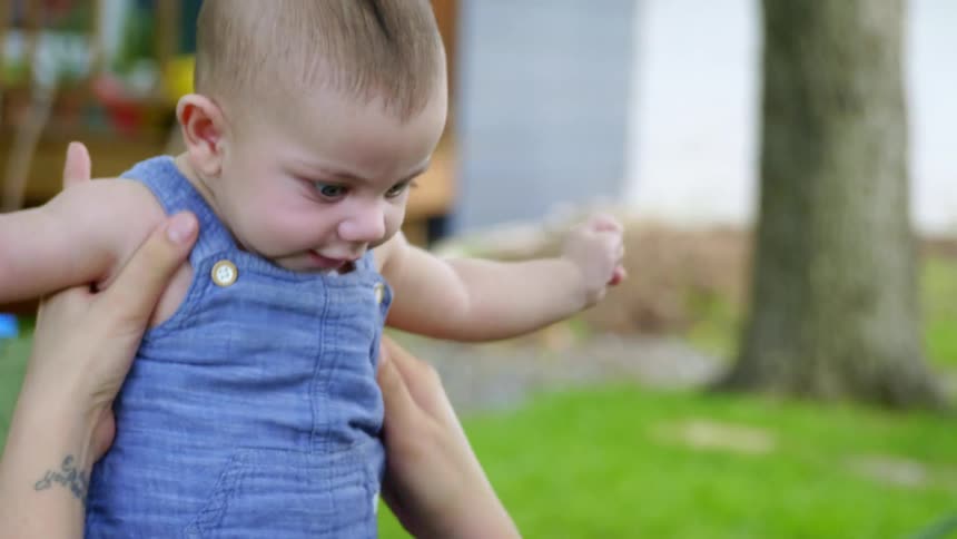 Person lies on back in hammock in yard holding baby