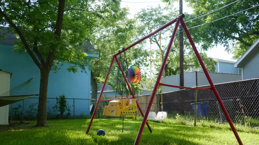 Tree standing in yard casts shadow across swing set with pinwheel