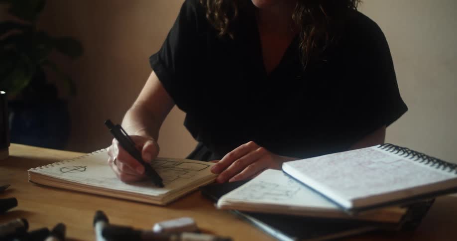 A woman with glasses sitting at a table marking on a notebook