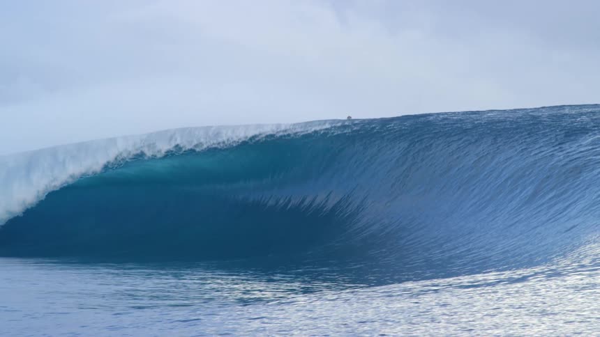 A group of people ride a large wave in the ocean as a boat passes by