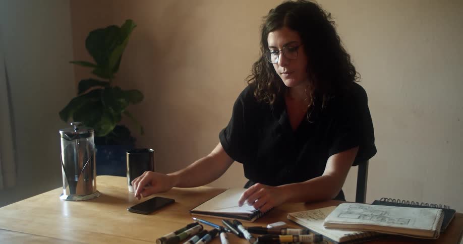A woman sitting at her desk looks at her cell phone and puts it down and picks up a marker