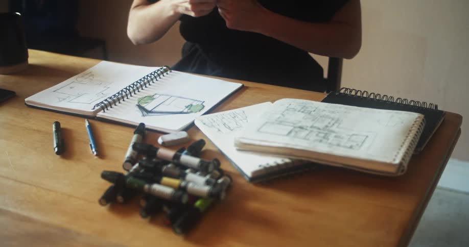 A woman puts down a marker and picks up another as she works on a house sketch in a notebook