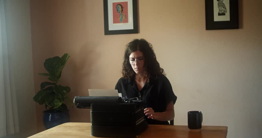 A woman sits at a table and types on a typewriter