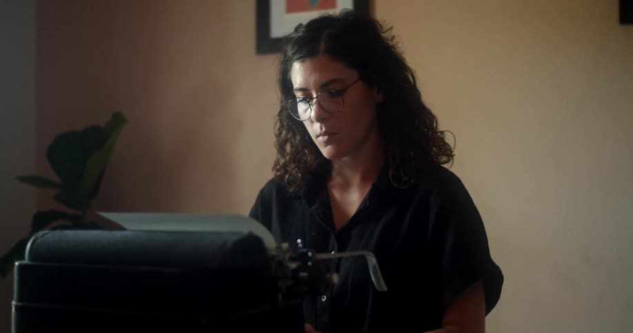 A woman wearing eyeglasses uses a typewriter while sitting at a desk