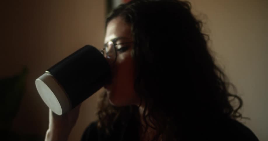 A woman takes a drink from a mug as she sits at a table with a notepad
