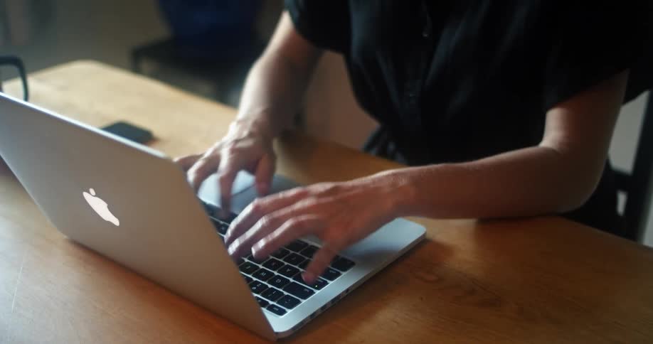 A woman sitting at her desk sets down her cellphone and begins typing on her laptop