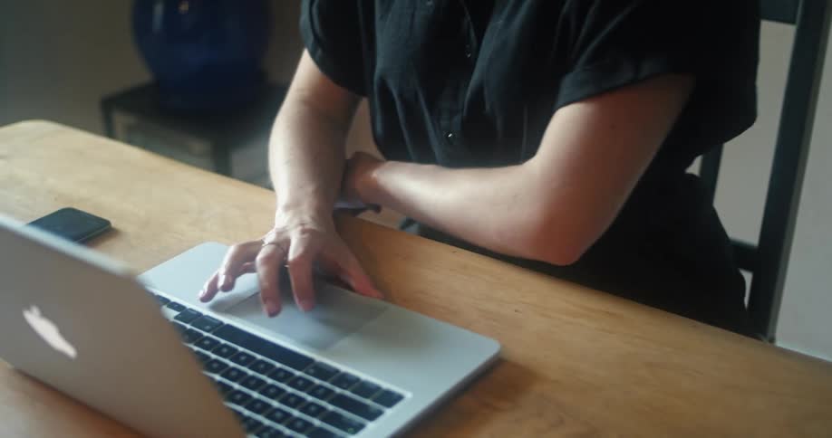 The woman drinks from the mug while using a laptop