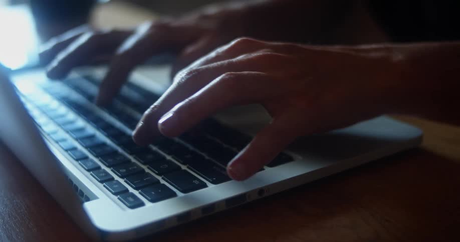 Fingers type on a laptop keyboard with a coffee cup near by