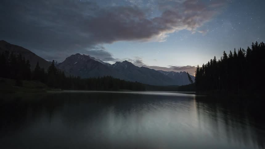 A lake reflects a mountain ridge and clouds on its surface as the sun rises
