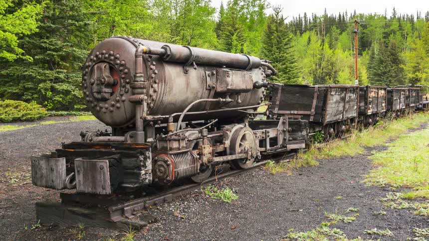 A vintage train car and tracks sit near a forest