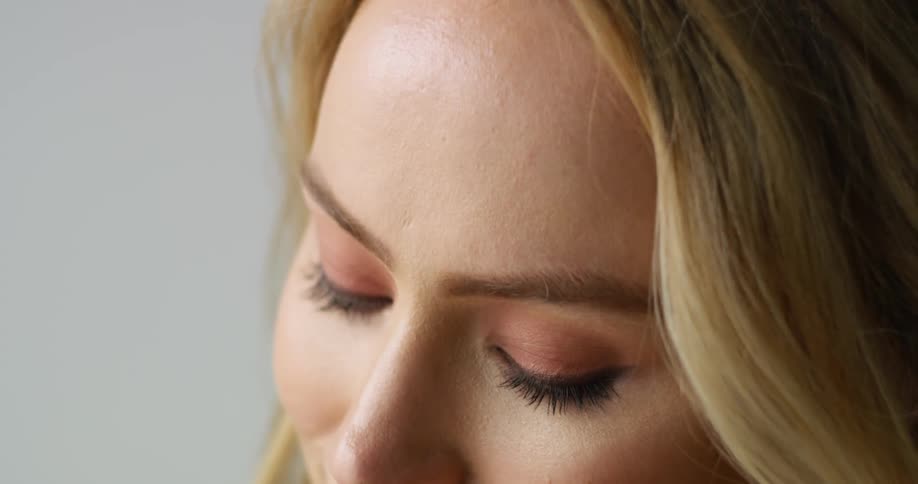 A woman with blonde hair is looking upwards before looking down and smiling