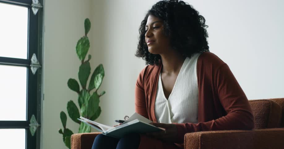 A black woman sits in a chair with a book and smiles