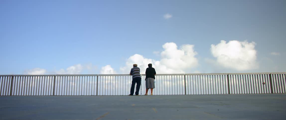 Couple leans against railing looking past it as ball bounce up nearby