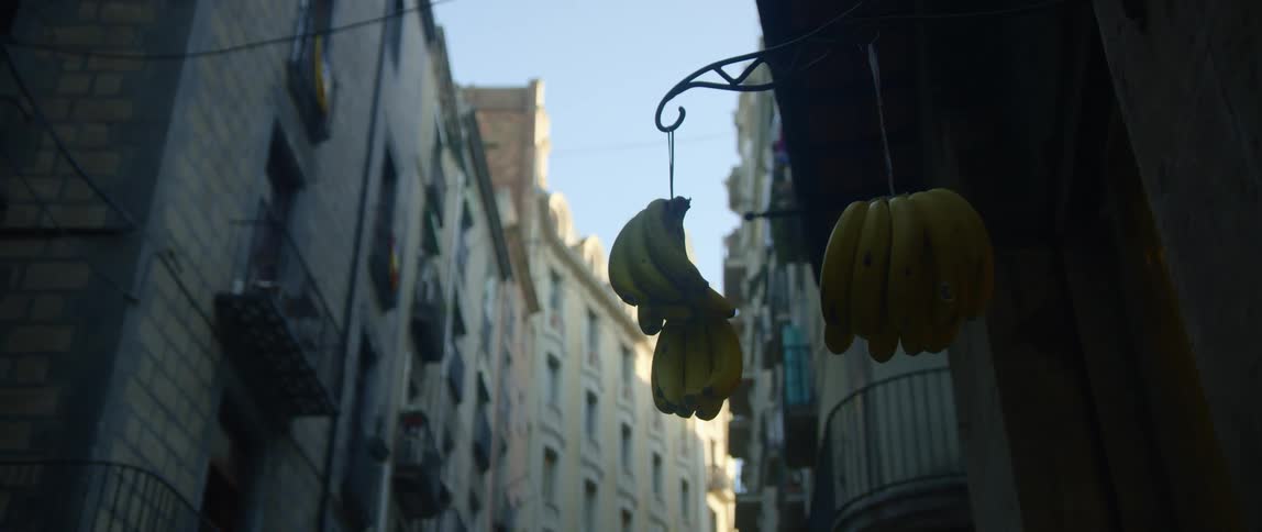 Bananas hang outside apartment buildingin neighborhood under clear blue sky