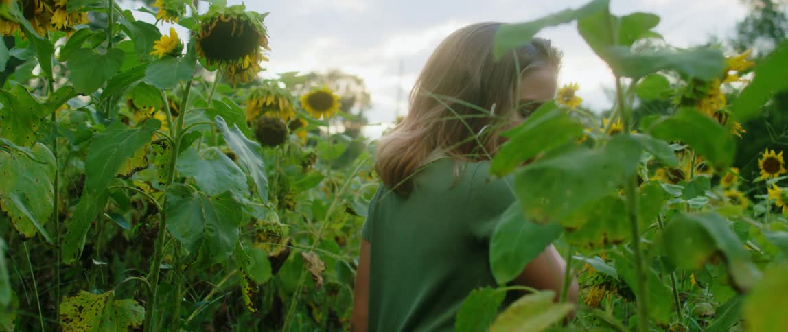 A girl examines flowers in a field of tall vegetation