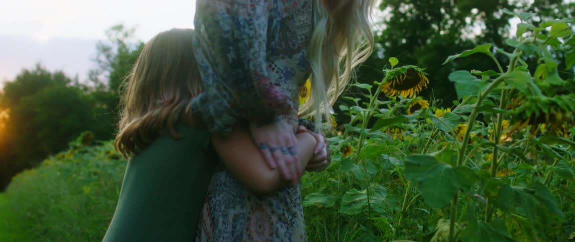 A girl hugs a woman by the sunflower patch