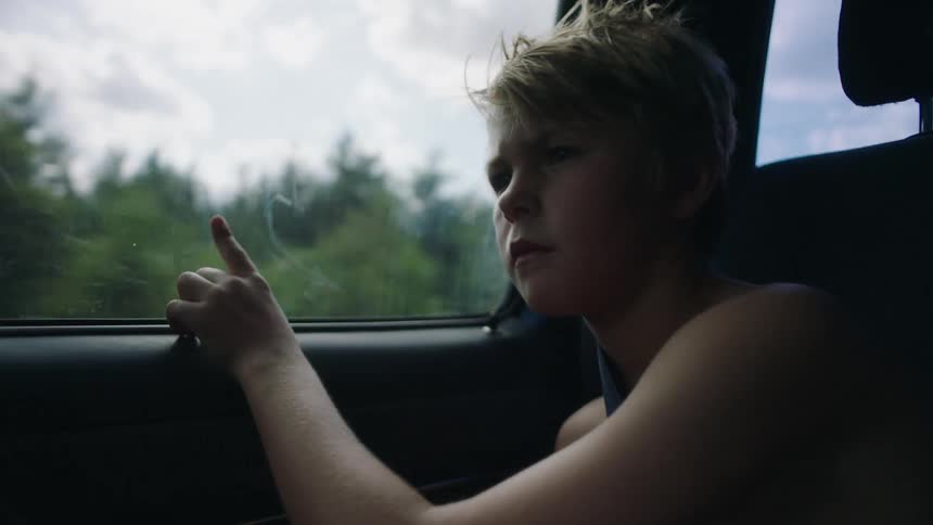 Blonde child looking bored sits on a front seat of the moving car