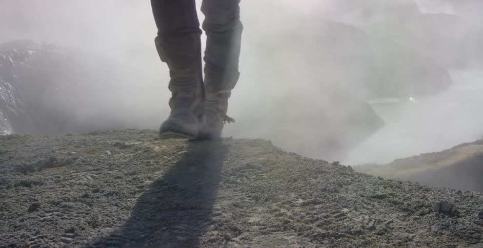 A person wearing boots walks through the steam coming out of hot springs