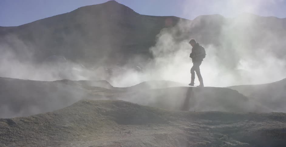A photographer standing in a field of geysers takes a photograph of his surroundings before walking onward