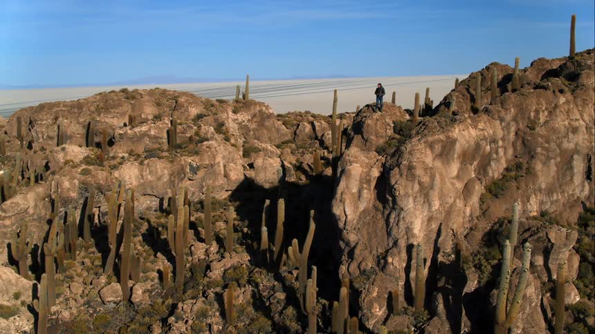A photographer takes a photo while standing atop a rock formation in the desert
