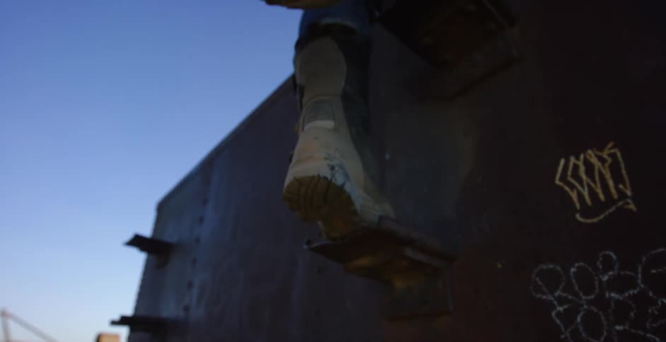 A man climbing up a rusted piece of metal in the desert