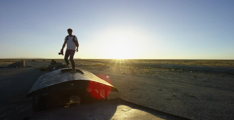 A photographer walks across the top of a derelict train on a sunny day