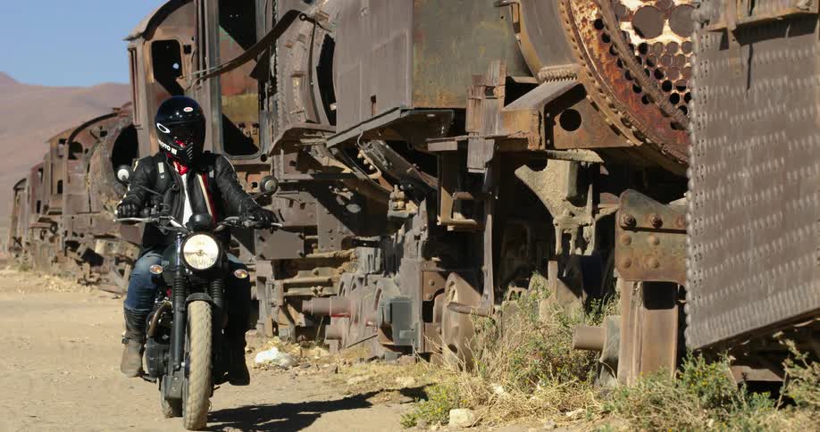 A man riding a motorcycle next to a rusted train in the desert
