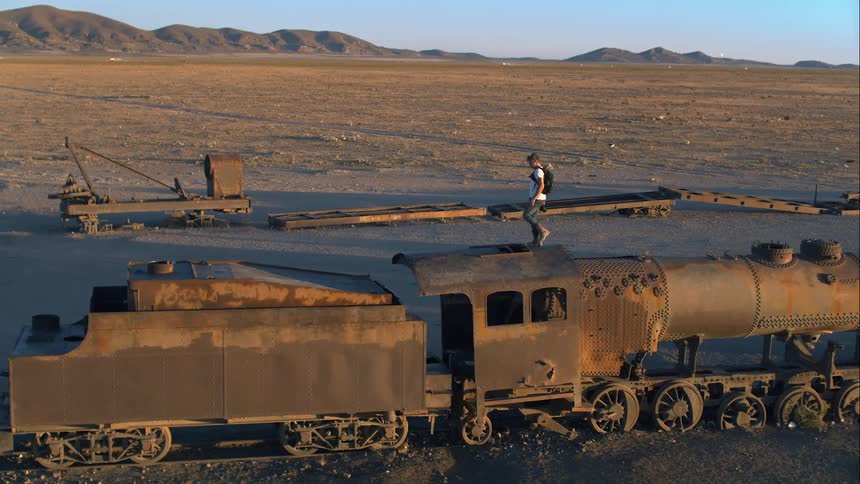 A photographer carries his camera as he walks atop a derelict train in the desert
