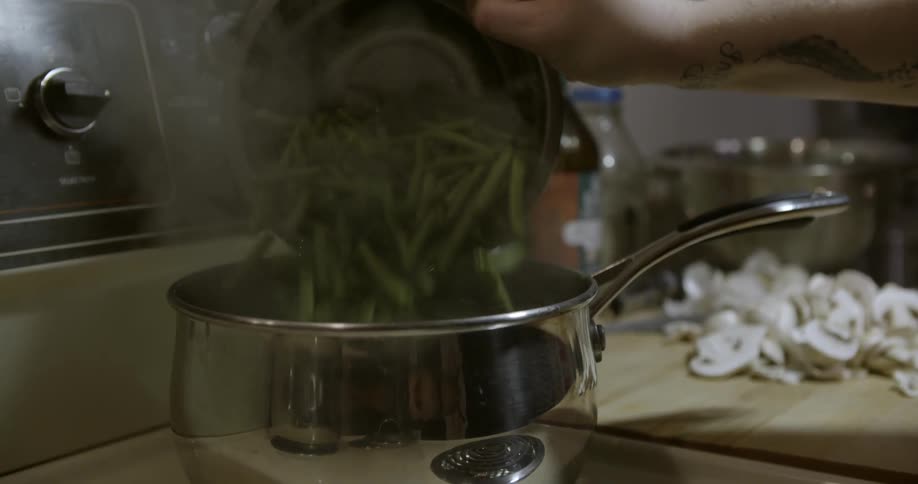 A woman removing the lid from a pot before dumping a bowl of green beans into the boiling water