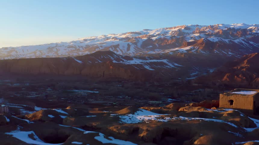A town next to a cliff with a snow covered mountain range and the sky in the background