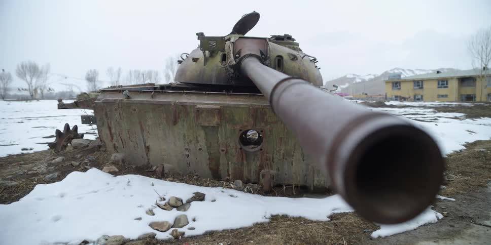 A derelict tank in a snowy field stands with its barrel facing the camera