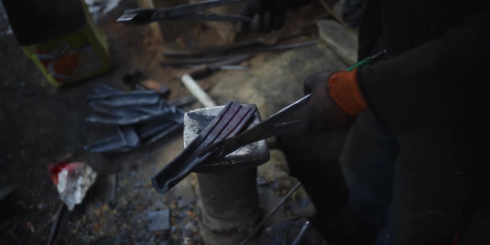 Two workers hammer a piece of hot metal on an anvil in a workshop