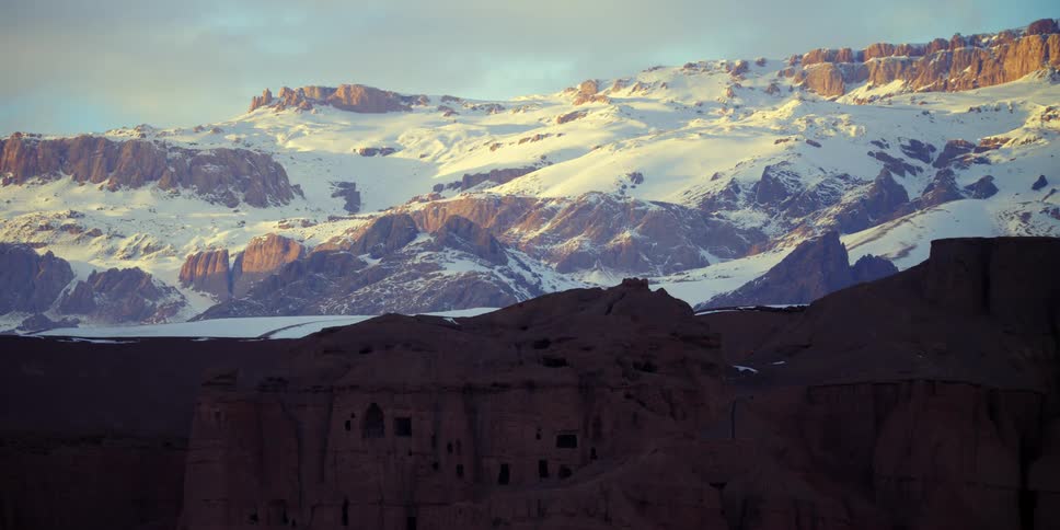 A building is carved into a mountain side located near the base of snow covered mountains