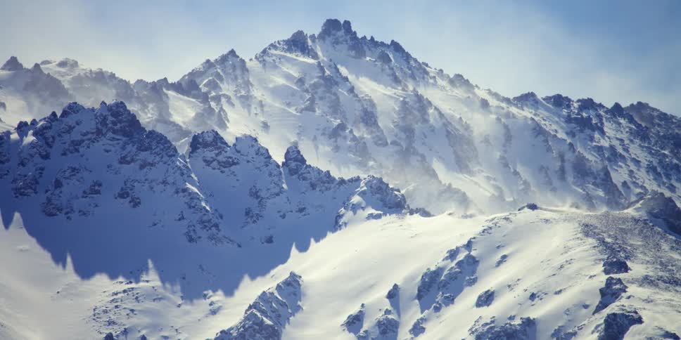 The snow blows around on the mountain range