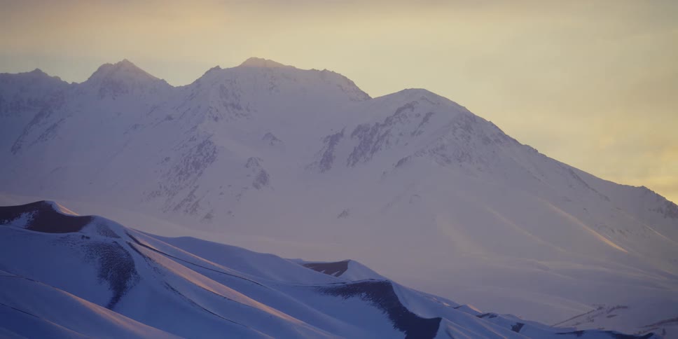 A snow covered mountain ridge on a cloudy evening