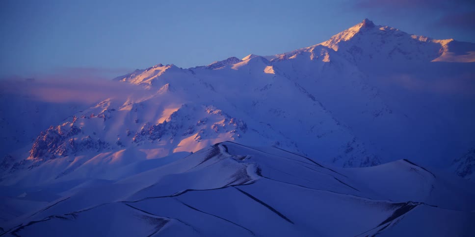 Snow covered mountain ridge peaks over scattered clouds