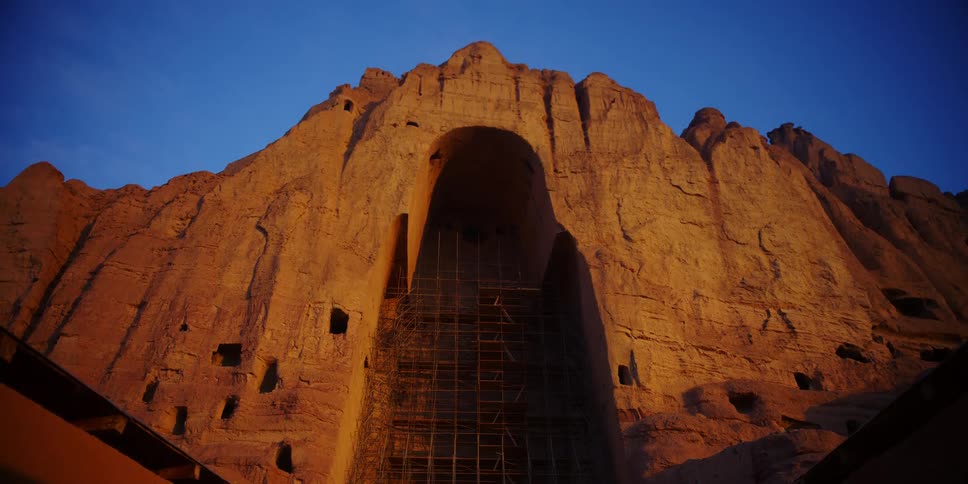 A cliff with carvings with a bird flying by with the sky and clouds above