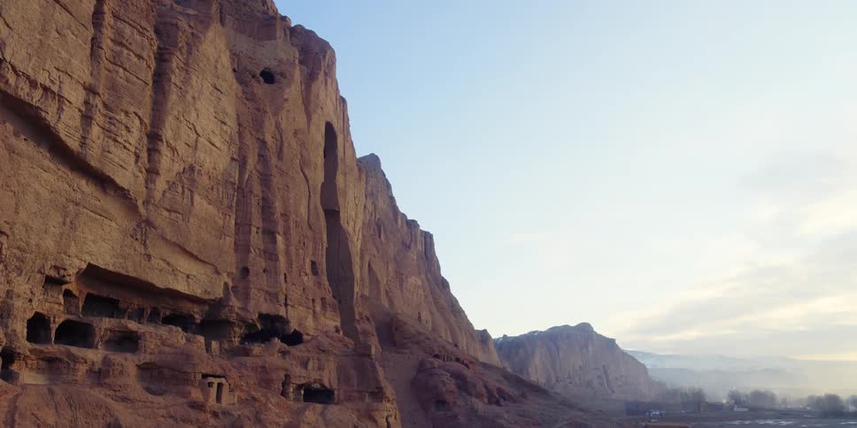 A cliff in the desert with trees the sky and clouds in the background