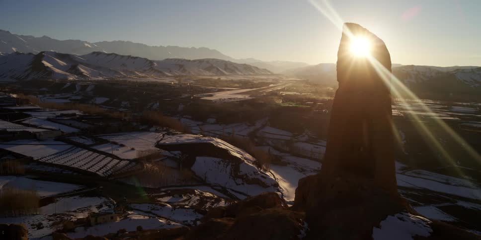 A town near a cliff with snow with a mountain range and the sky in the background