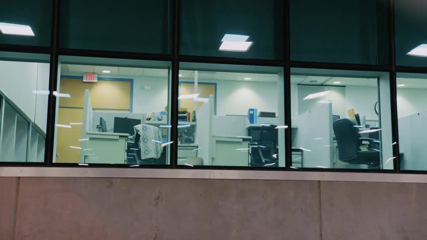 Empty office cubicles through building windows at night