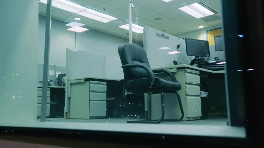 Cubicles in an office are empty at night and viewable from outside with floor to ceiling windows