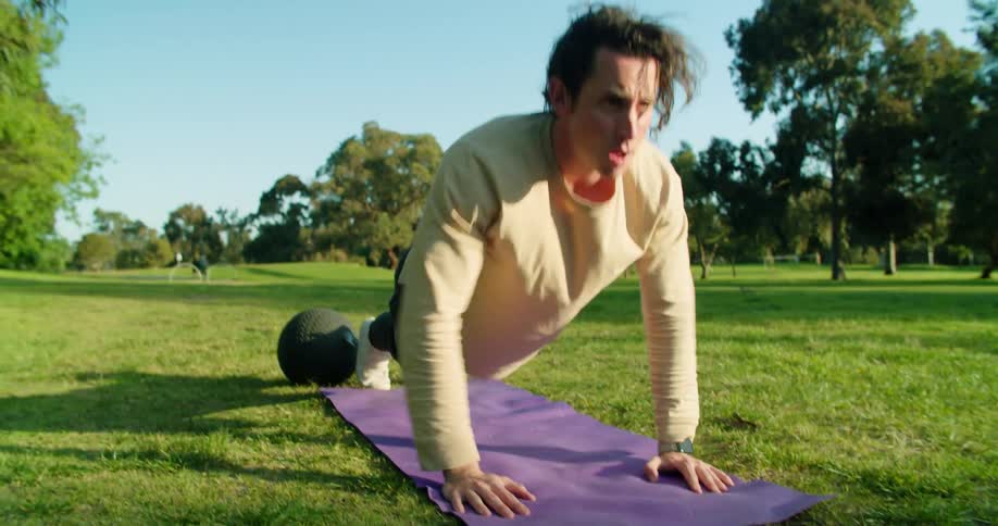 A man performs a series of push ups in the middle of a grass field in a park