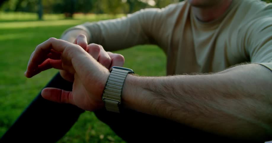 A man is sitting in the grass and looking at his watch