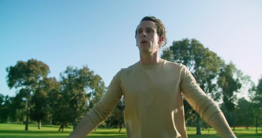 A white man stands in a park and stretches his arms