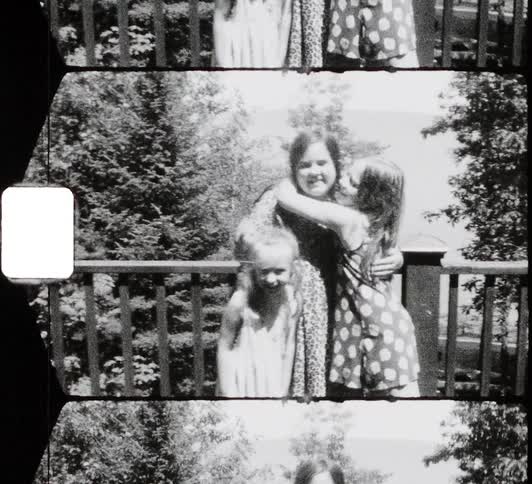 Three young white girls stand in front of a wooden railing outdoors and hug smile and kiss