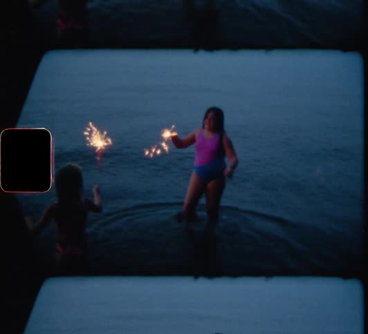 A pair of girls play with sparklers while standing in the shallow waters of the beach at night
