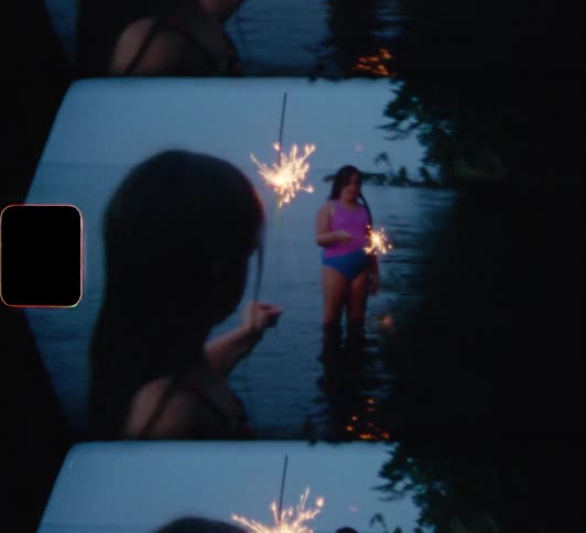 Three girls walking in a lake while holding sparklers with the sky in the background