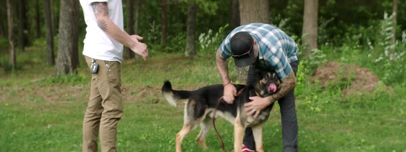 A man holds on to a dogs leash while another man pets the dog then takes the leash away from him