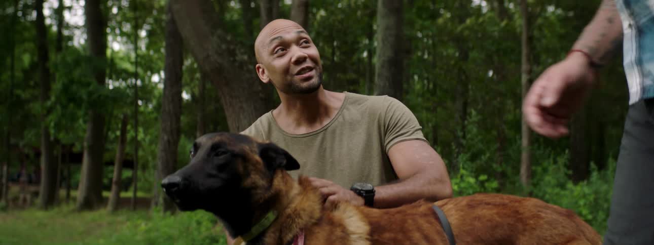 A man kneels down to pet a dog with another man standing beside them also petting the dog